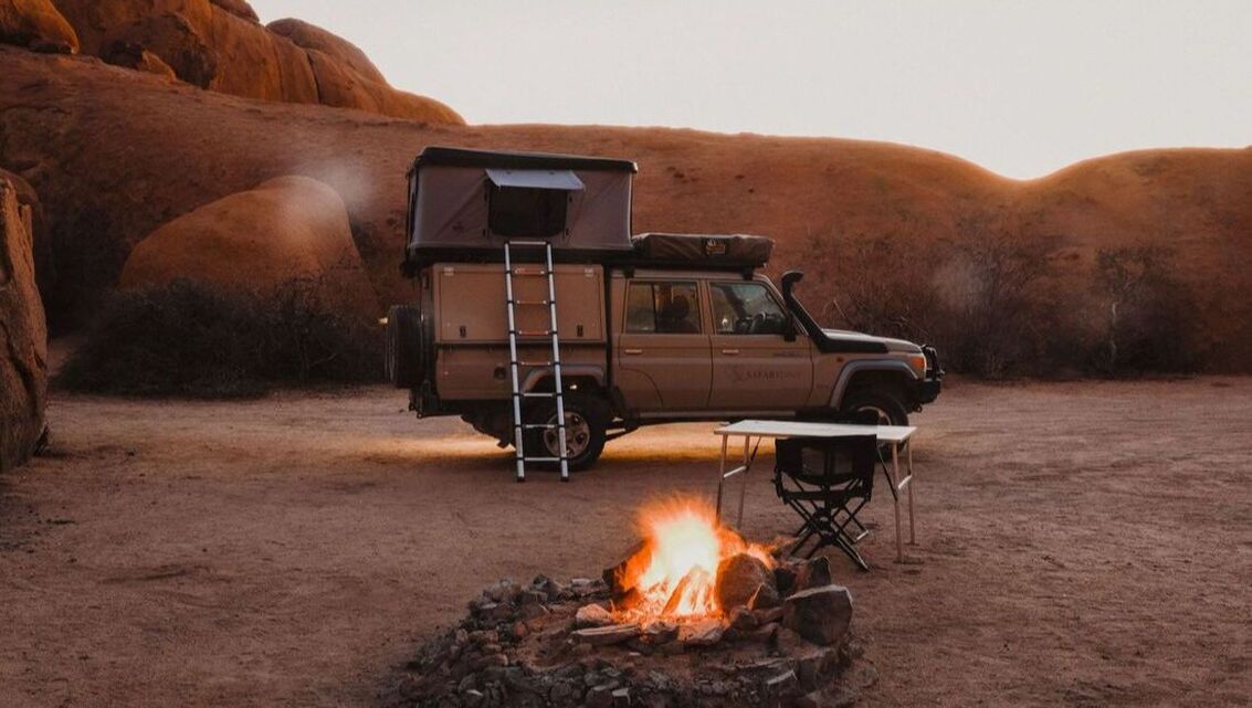 Ein Safarifahrzeug steht neben einem Fahrzeug in einer kargen Wüstenlandschaft