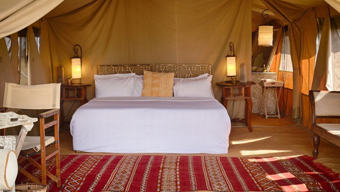 Ein gemachtes Doppelbett in einem großen Zelt mit Teppich