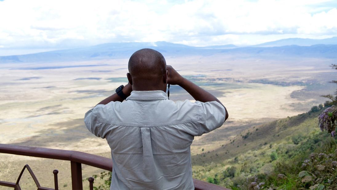 Ein Mann mit einem Fernglas schaut von einer Aussichtsplattform auf eine weite Ebene hinab