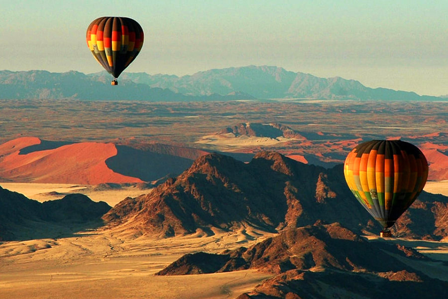 Zwei Heißluftballons fliegen über den Dünen und der Wüste in Namibia