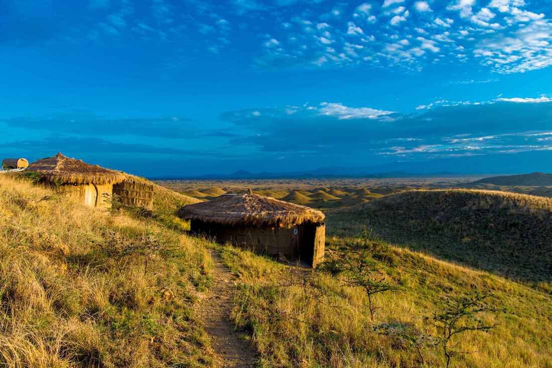 Zwei Stohhütten auf einem Hügel mit Ausblick über die Savanne