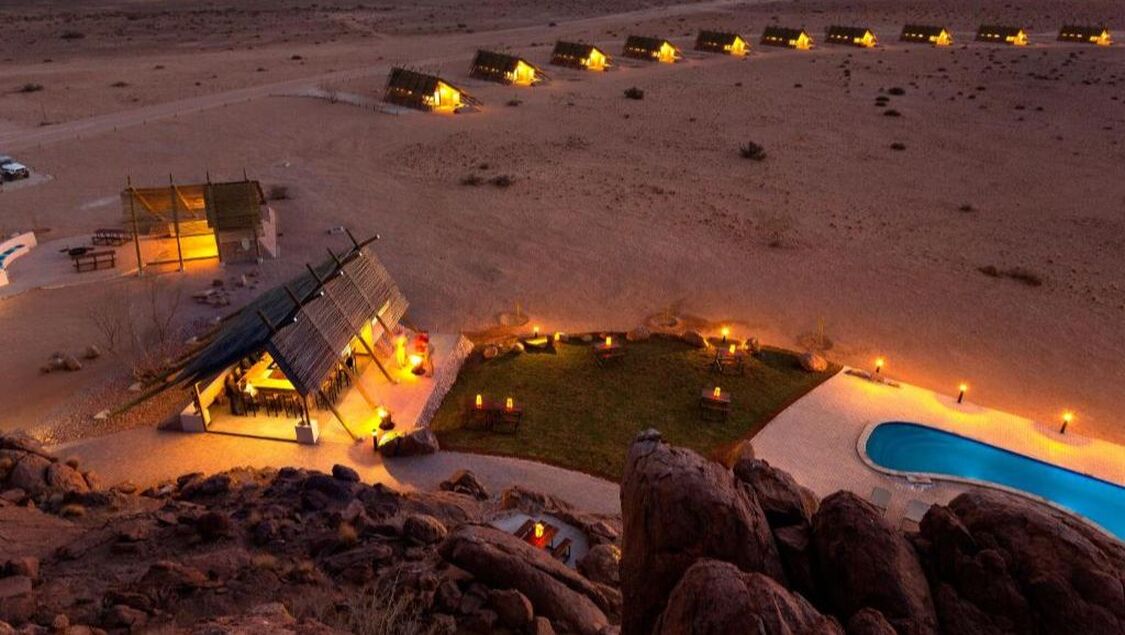 Ein mit Fackeln beleuchtetes Camp in der Namibischen Wüste in der Abenddämmerung