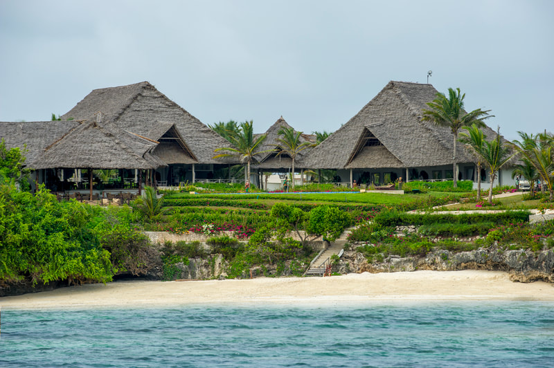 Mehrere Gebäude mit Palmendach stehen neben einem Strand am Meer
